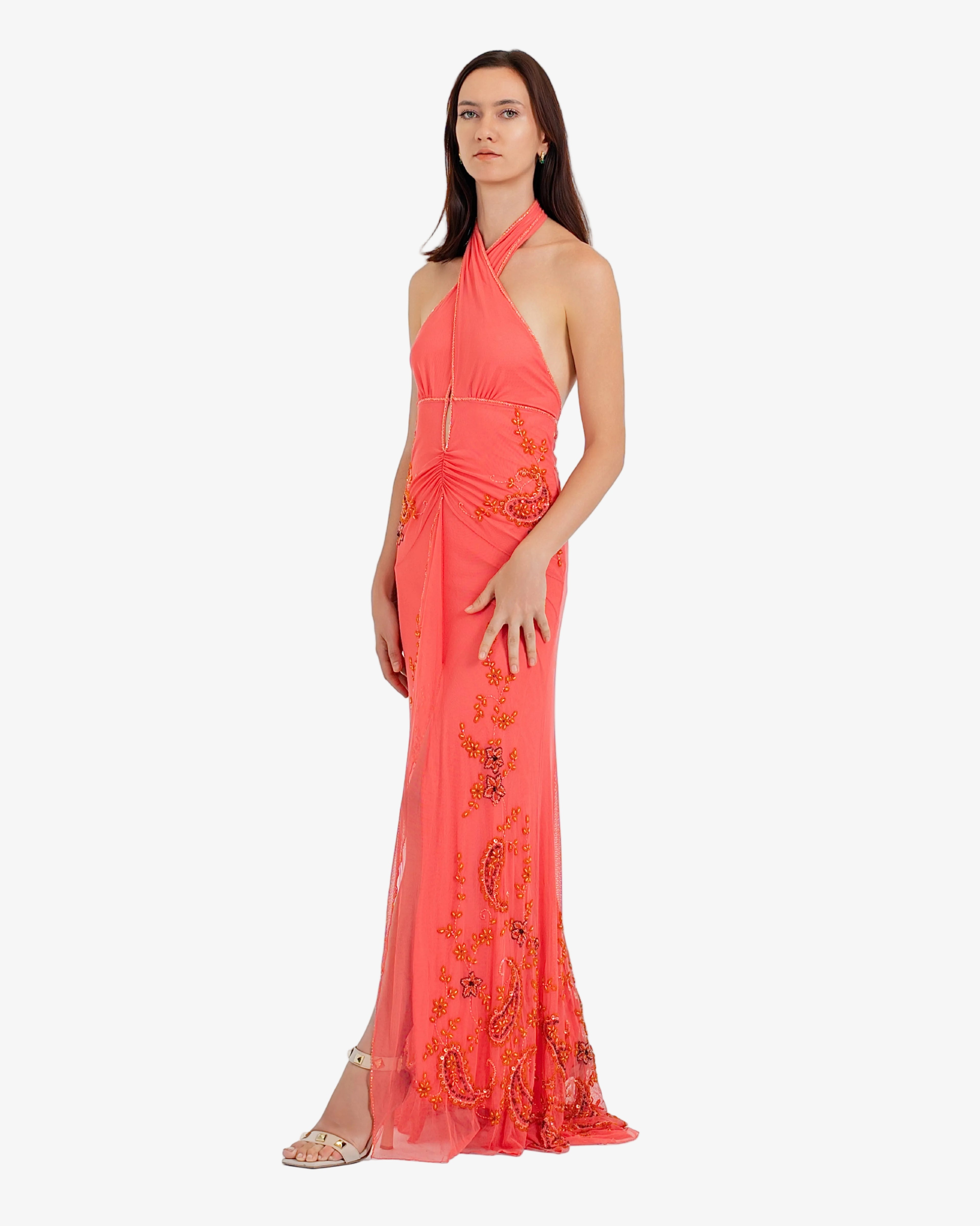 Woman wearing a coral evening gown with floral embroidery on a white background